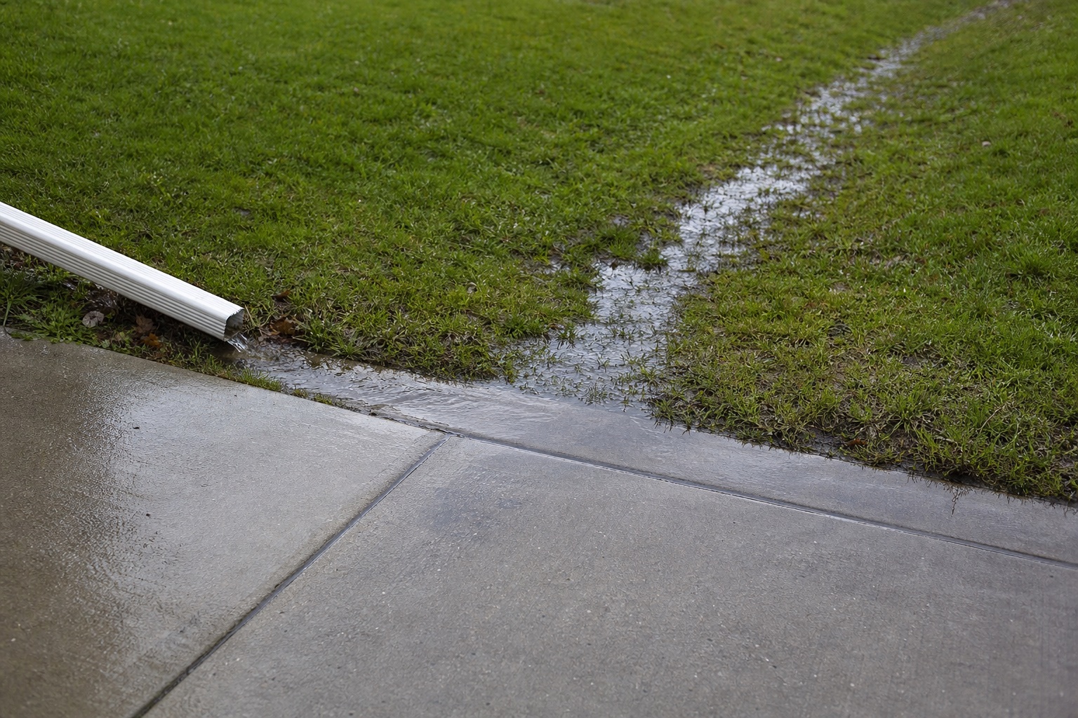 Illustrative view of rainwater moving from a downspout beside a concrete walkway